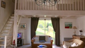 Uma sala de estar com sofá, poltrona de vime, lustre, escada e um quadro na parede.