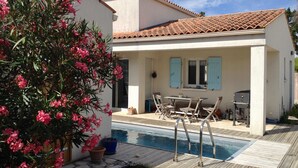 Uma área junto à piscina, com cadeiras de sol, móveis de exterior e um vaso de planta.