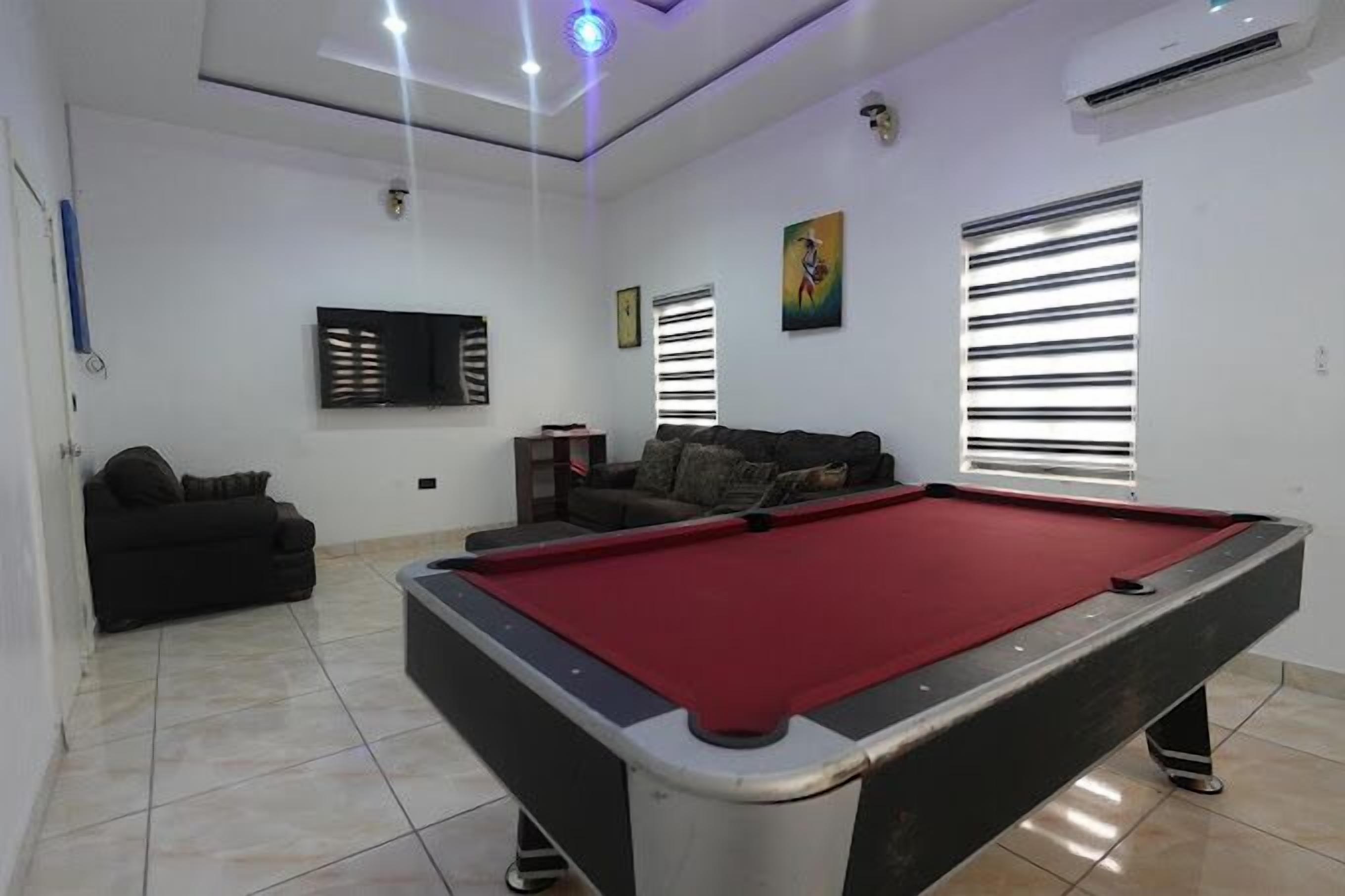 A pool table in a room with a sofa and a window with blinds.