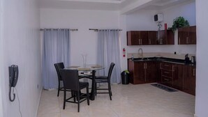 A dining area with a round table and chairs, a kitchen with wooden cabinets, and a phone on the wall. - Bamgbose Apartment  (Lagos)