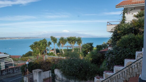 Ein Küstenanwesen mit einer Treppe, die zu einem Balkon mit Blick auf das Meer und einen fernen Berg führt.