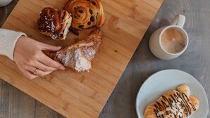En skärbräda i trä med bakverk och en kopp kaffe på ett bord.