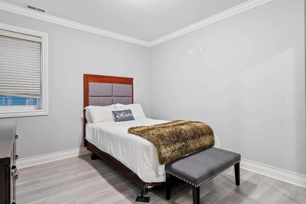 A bedroom with a bed, a bench, a window, and a door.