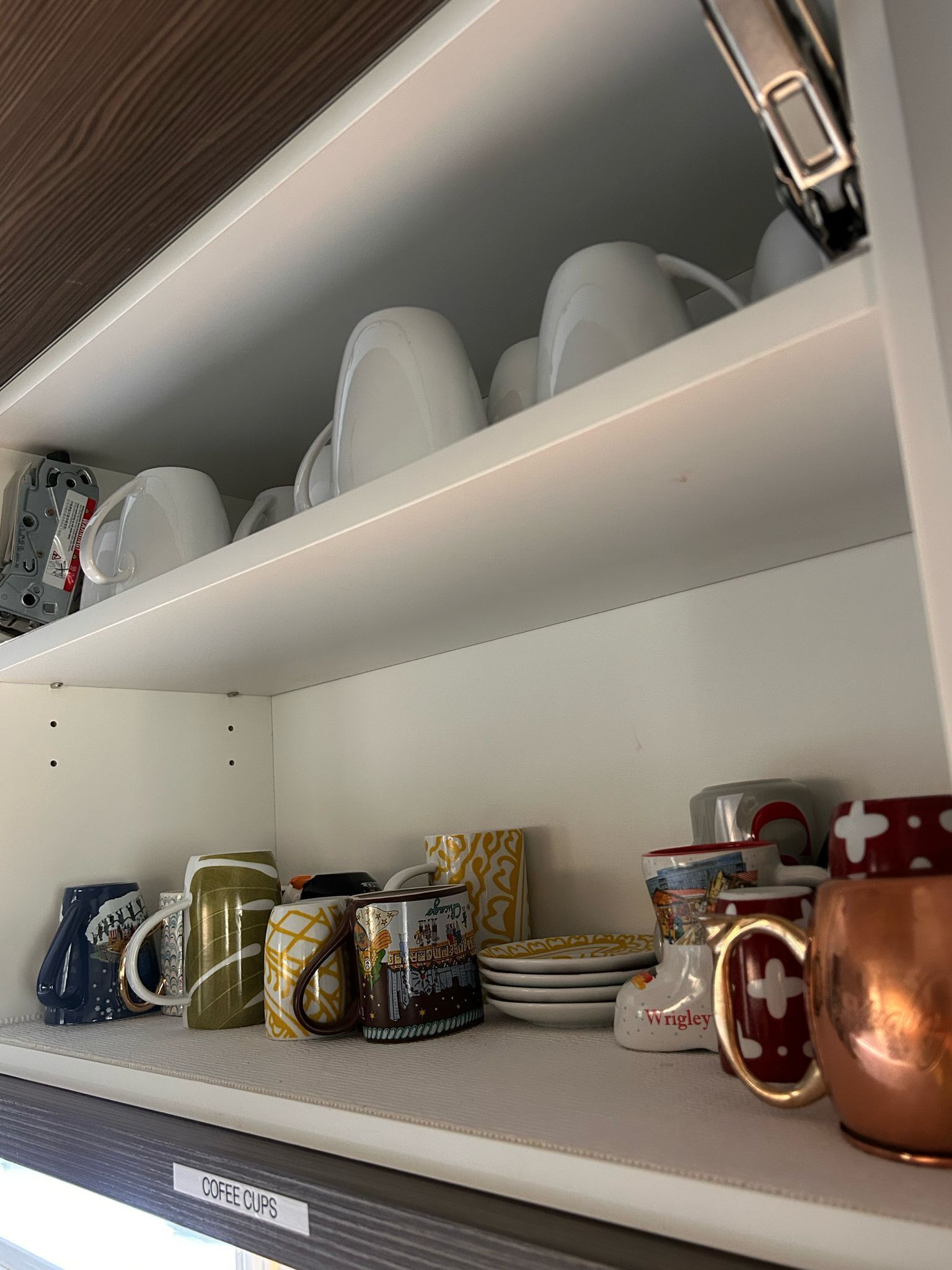 Une étagère avec divers gobelets et tasses à café, certains ornés de motifs et d’autres unis.