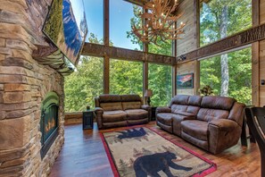 L’intérieur d’un chalet en bois, avec des murs en pierre, une cheminée, des canapés en cuir et de grandes fenêtres donnant sur la forêt.