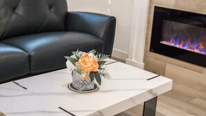 En moderne stue med en sort lædersofa, et hvidt marmorbord med en dekorativ vase, og en pejs med en tv-skærm der viser ild.
