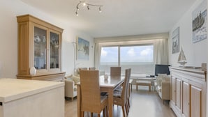 A spacious living area with a dining table, chairs, a large cabinet, and a television. - Flat in Blankenberge With Ocean Views (Blankenberge)