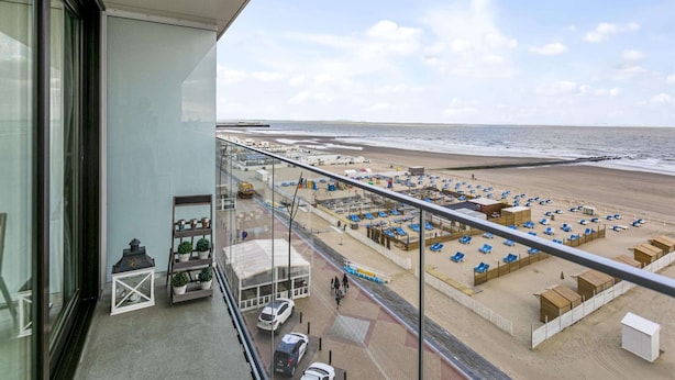 A balcony with a view of a beach, including lounge chairs and umbrellas. - Flat in Blankenberge With Ocean Views (Blankenberge)