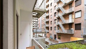 A balcony with a wooden table and chairs, overlooking a brick building with multiple balconies and fire escapes. - Flat in Blankenberge Near Belgium Pier (Blankenberge)