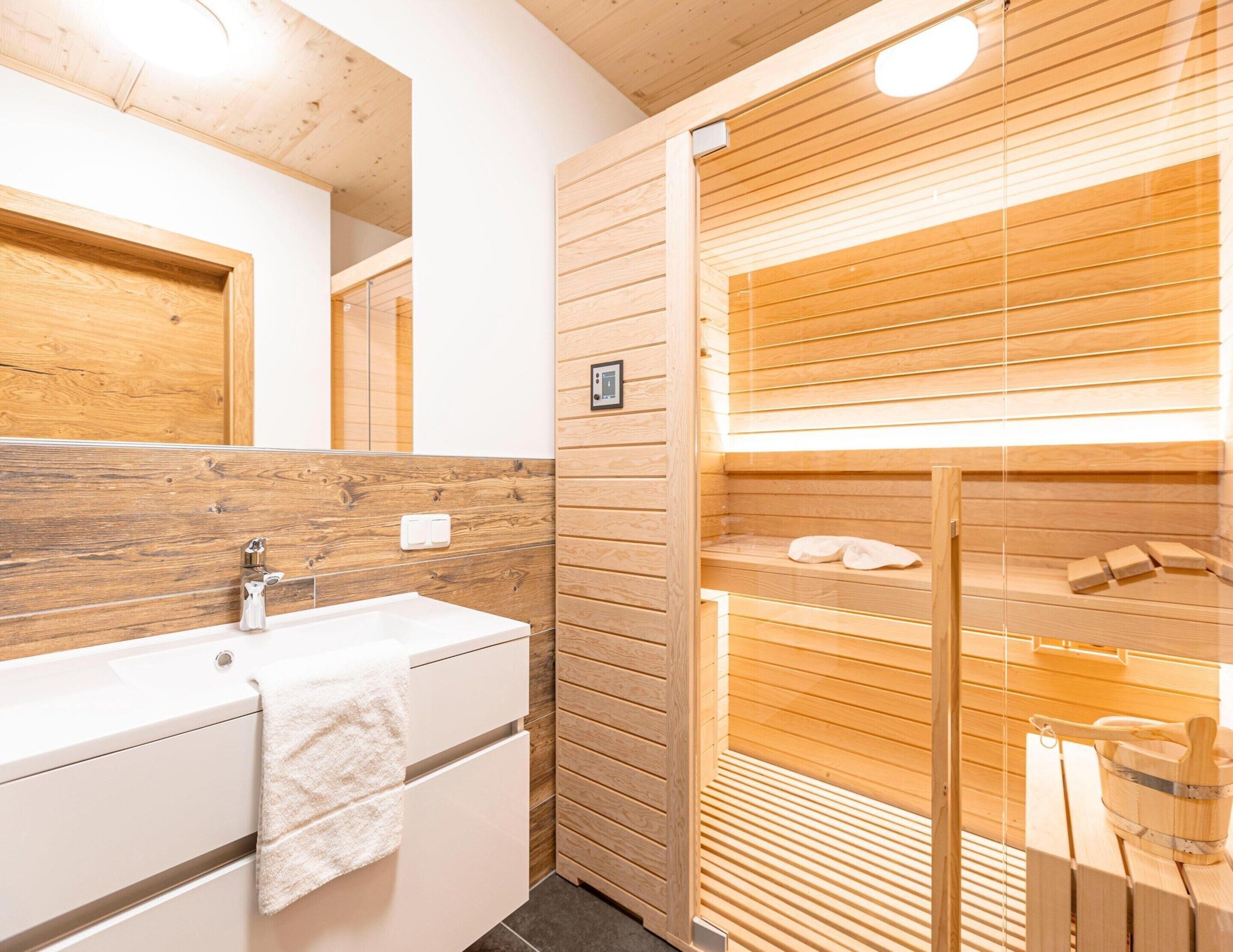 A modern bathroom with a wooden vanity, a mirror, and a glass-enclosed sauna area.