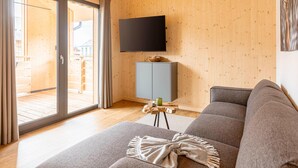A modern living room with a grey sofa, a flat-screen TV mounted on the wall, and a sliding glass door leading to an outdoor area. - Attractive Apartment With Sauna (Sankt Georgen am Kreischberg)
