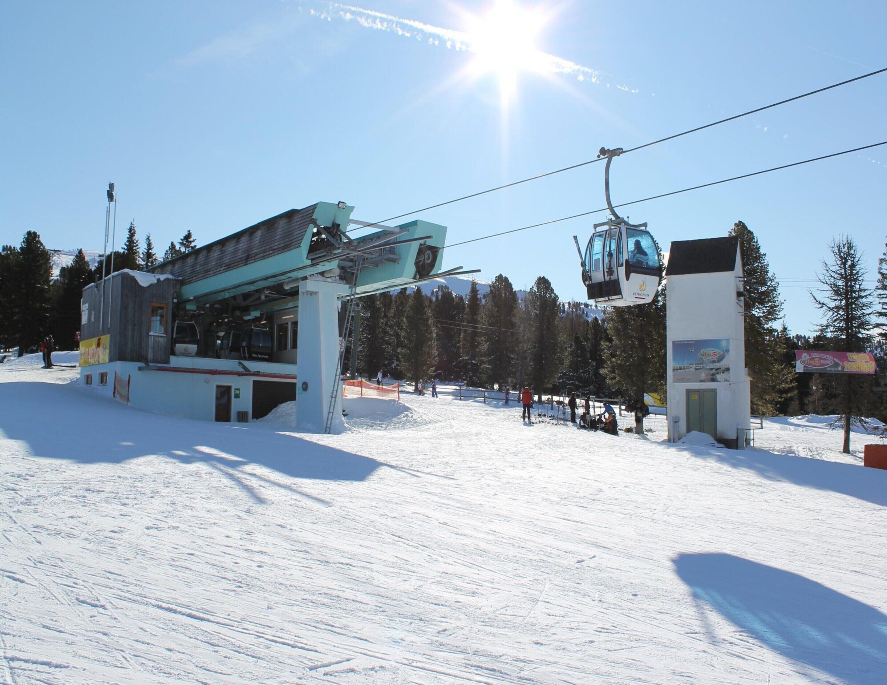 Eine Sesselbahnstation mit Skipiste, verschneitem Gelände und blauem Himmel.