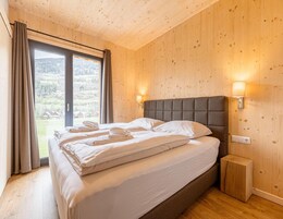 A bedroom with a large bed, wooden walls, a window with curtains, and a nightstand.