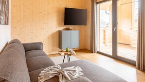 A modern living room with a wooden interior, a grey sofa, a small wooden table with a candle, and a TV mounted on the wall. - Attractive Apartment With Sauna (Sankt Georgen am Kreischberg)