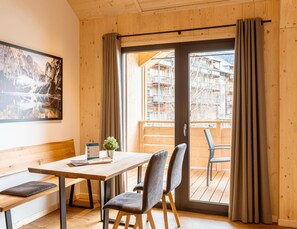 Un interior de madera con una mesa y sillas, un banco, una puerta con cortinas y un cuadro en la pared.