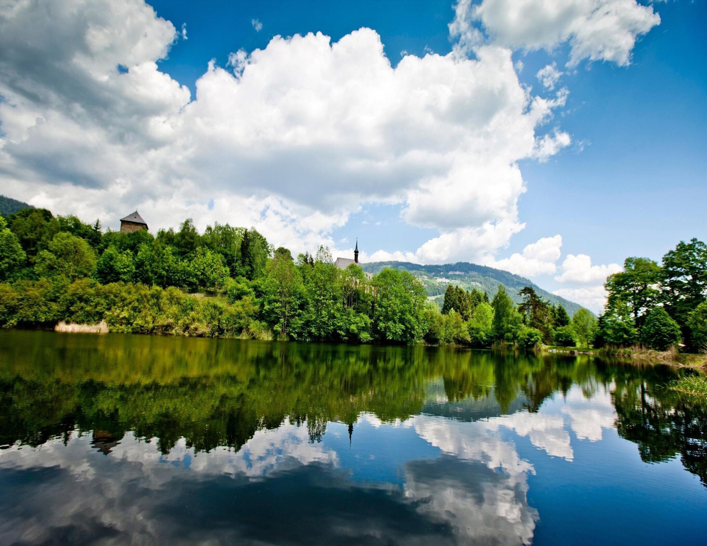 A serene landscape with a calm lake reflecting the sky and surrounding greenery.