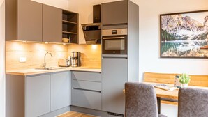 A modern kitchen with grey cabinets, a wooden countertop, and a built-in oven. There is a dining area with a wooden table and two chairs. A painting of a mountainous landscape is on the wall. - Attractive Apartment With Sauna (Sankt Georgen am Kreischberg)