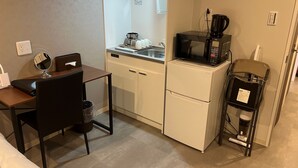 A compact kitchenette with a microwave, coffee maker, and a small refrigerator. There is a dining table with a chair and a mirror.