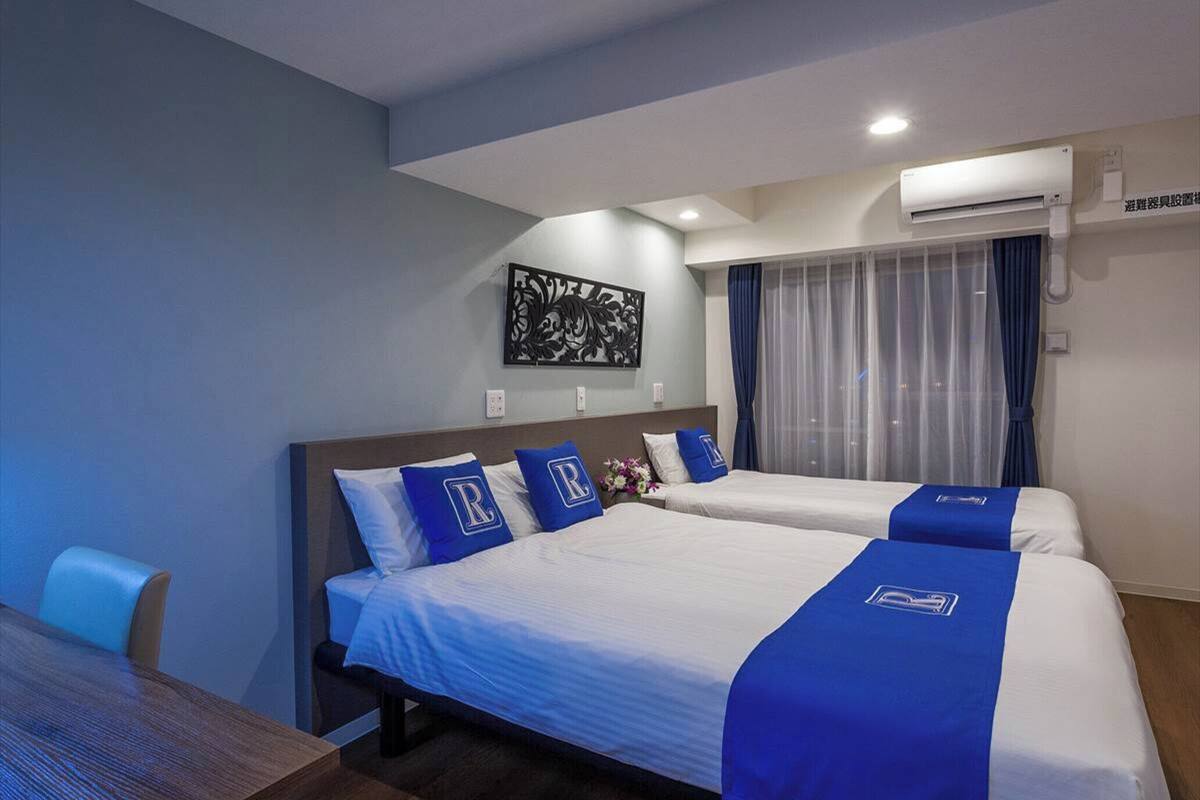 A hotel room with two beds, a dining table, and a decorative wall piece.