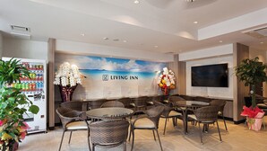 A Living Inn reception area with wicker furniture, a vending machine, and a large TV screen.
