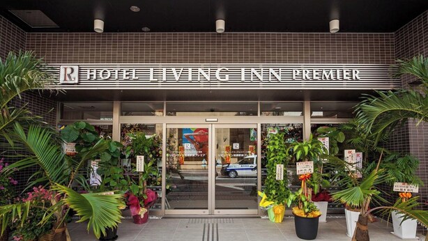 The entrance of Hotel Living Inn Premier with a tiled facade, large potted plants, and a clear view of the interior through the glass doors.