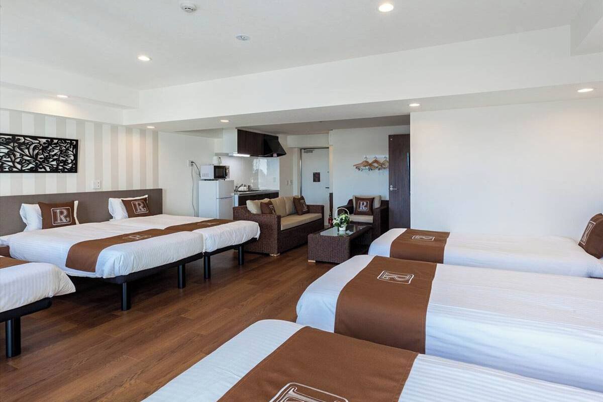 A hotel room with three beds, a kitchenette, and a seating area.