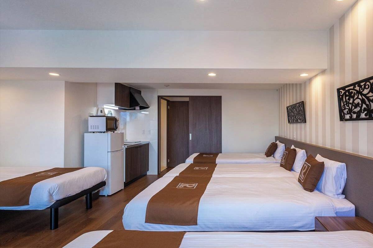 A hotel room with two beds, a kitchenette, and a separate bathroom.