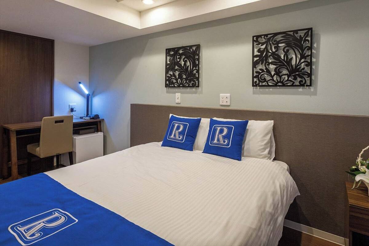 A hotel room with a bed, a desk, and two wall-mounted decorative pieces.
