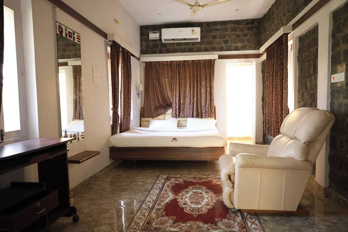 A bedroom with a bed, a chair, a desk, and a patterned rug.