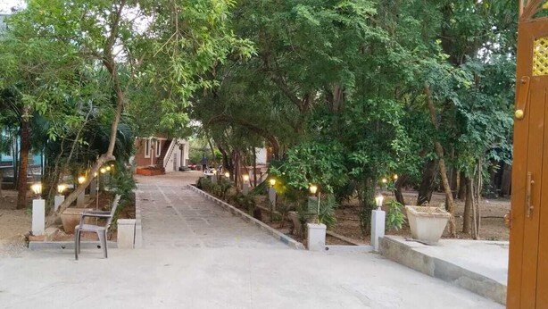 Un sendero que atraviesa un jardín con árboles y bancos, y un edificio al fondo.