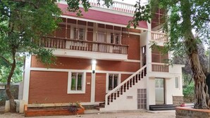 Un edificio de dos pisos con una escalera que conduce al nivel superior, rodeado de árboles.