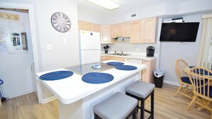 A modern kitchen with a central island, wooden cabinets, a built-in oven, and a wall-mounted TV. - Coral Ridge 1-Oceanside 78th St, Free WiFi, W/D, AC (Ocean City)