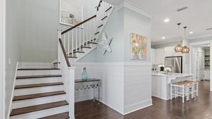 A modern kitchen with white cabinetry, a stainless steel refrigerator, and a dining area with white chairs. - Family Tides FREE 6-Seater Golf Cart,and 5 Bikes!! 2 Resort Pools, Pickleball Courts (Santa Rosa Beach)