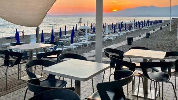 An outdoor seating area with tables and chairs, overlooking a beach with umbrellas and lounge chairs. - ITALY VILLAGE (Sessa Aurunca)