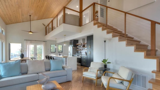 A spacious living area with a high ceiling, a staircase, and a modern kitchen. - Experience ocean views at Pelican Brief, a spacious 4-bedroom house in Oak Island! (Oak Island)