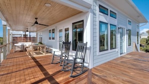 A covered wooden deck with outdoor furniture, large windows, and a ceiling fan. - Experience ocean views at Pelican Brief, a spacious 4-bedroom house in Oak Island! (Oak Island)