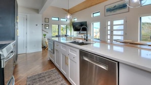 A modern kitchen with a large island, stainless steel appliances, and a wooden ceiling. - Experience ocean views at Pelican Brief, a spacious 4-bedroom house in Oak Island! (Oak Island)