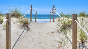 A sandy beach with wooden posts and ropes, leading to the ocean. - Experience ocean views at Pelican Brief, a spacious 4-bedroom house in Oak Island! (Oak Island)