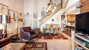 Un ampio soggiorno con soffitto alto, una zona pranzo con sedie di legno, un divano in pelle e una scala che conduce a un piano superiore.