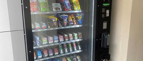 A vending machine with various snacks and drinks, including brands like Takis and Skittles, and a payment interface with a card slot and a keypad.