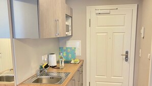 Uma cozinha compacta com geladeira embutida, micro-ondas e pia. Possui bancada de madeira e uma porta que dá para outro cômodo.