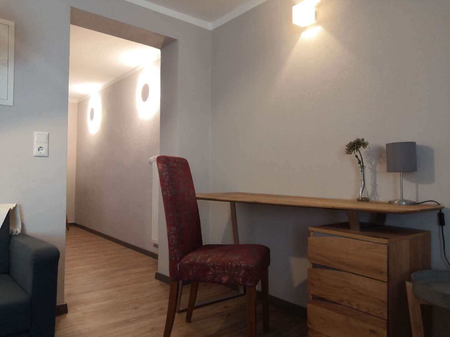 Une pièce avec un bureau en bois, une chaise rouge, une lampe et une petite plante.