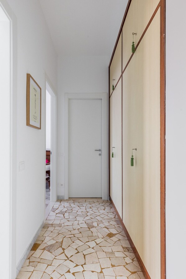 A hallway with a tiled floor, a white door, and a wooden wardrobe with a hanging green ornament.