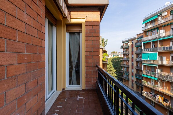 A narrow balcony with a brick wall on one side and a multi-story building on the other.