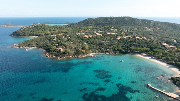 An aerial view of a coastal area with a beach, clear turquoise waters, and scattered buildings.