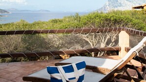 A sunlit outdoor seating area with a view of the sea and mountains.
