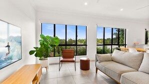 A modern living room with large windows, a wooden bench, a leather chair, and a beige sofa. - Cove Retreat - Kid Pet and Pool Paradise (Palm Cove)