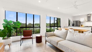 A modern living room with large windows, a sofa, a chair, and a small table. - Cove Retreat - Kid Pet and Pool Paradise (Palm Cove)