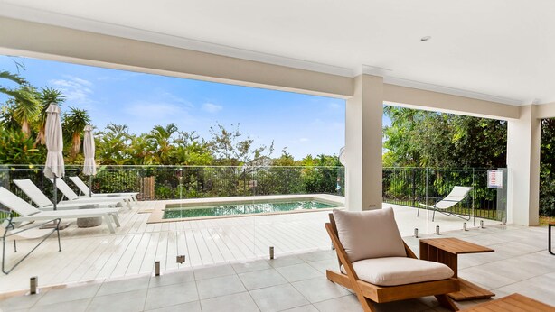 A modern outdoor pool area with lounge chairs, a wooden table, and a view of a tropical garden. - Cove Retreat - Kid Pet and Pool Paradise (Palm Cove)