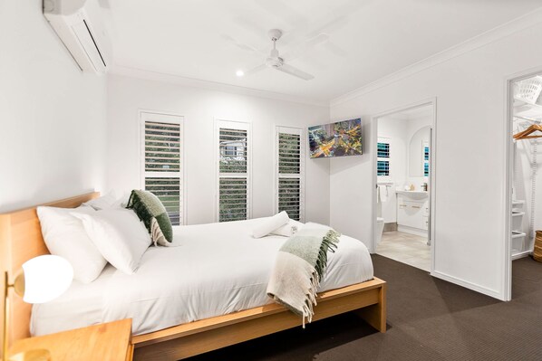 A bedroom with a bed, a ceiling fan, and a view of a bathroom through an open door. - Cove Retreat - Kid Pet and Pool Paradise (Palm Cove)